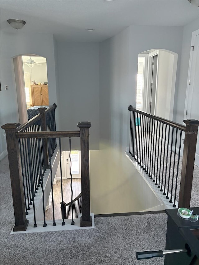 hall with arched walkways, carpet flooring, an upstairs landing, and baseboards