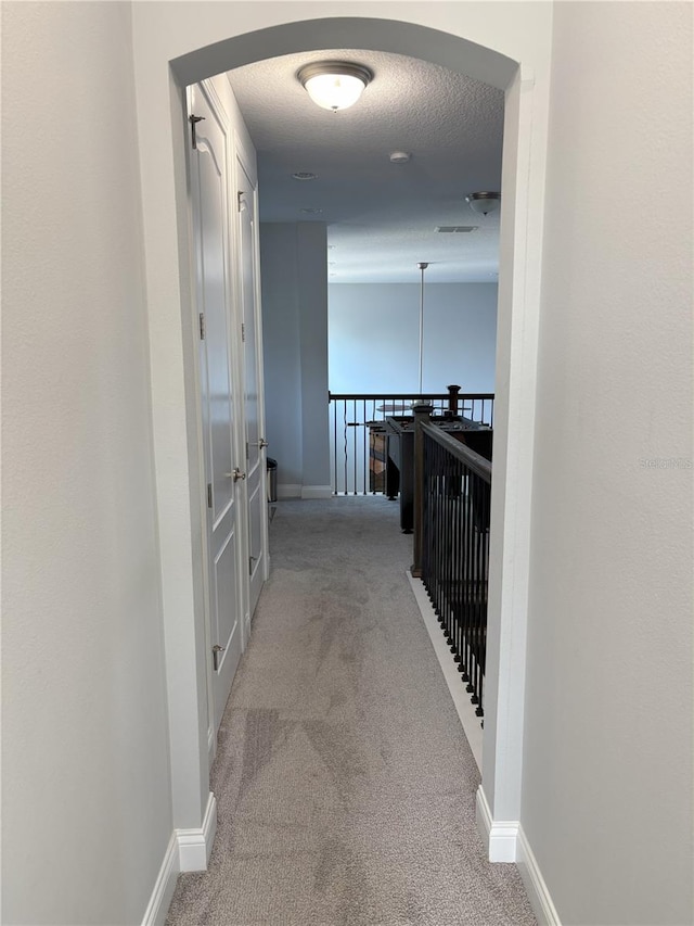 corridor with carpet floors, a textured ceiling, and baseboards