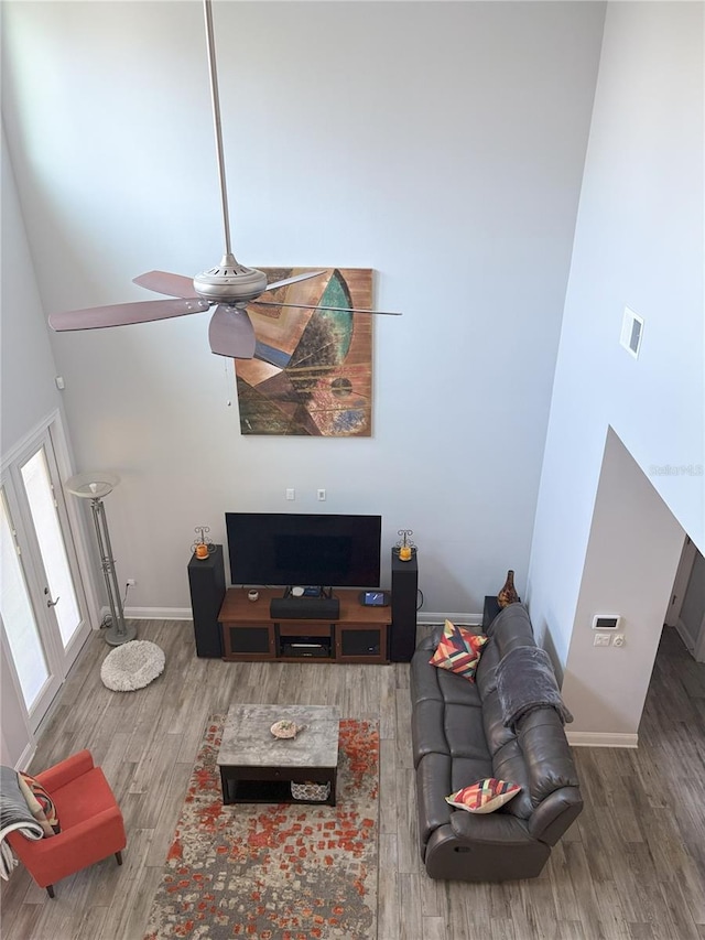 living area with visible vents, baseboards, a towering ceiling, ceiling fan, and wood finished floors