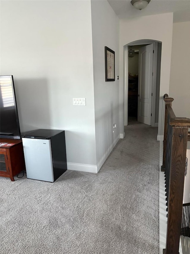 hall with arched walkways, light carpet, and baseboards