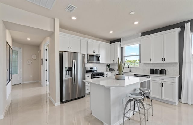 kitchen with a breakfast bar area, stainless steel appliances, light countertops, white cabinetry, and a kitchen island