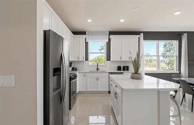 kitchen with white cabinets, a kitchen island, stainless steel appliances, light countertops, and a sink