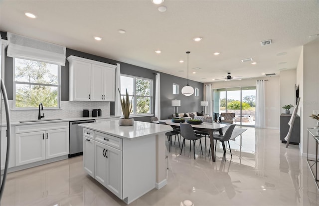 kitchen with a kitchen island, a sink, open floor plan, light countertops, and stainless steel dishwasher