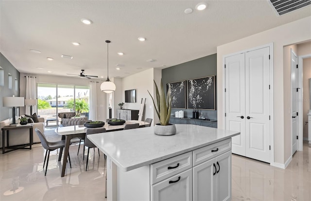 kitchen featuring decorative light fixtures, visible vents, open floor plan, white cabinets, and a kitchen island