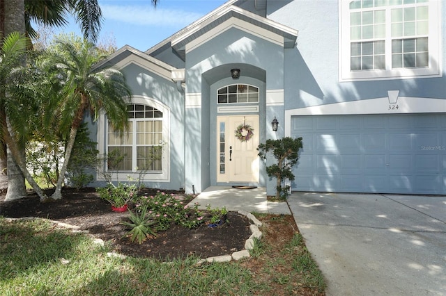 property entrance with a garage, driveway, and stucco siding