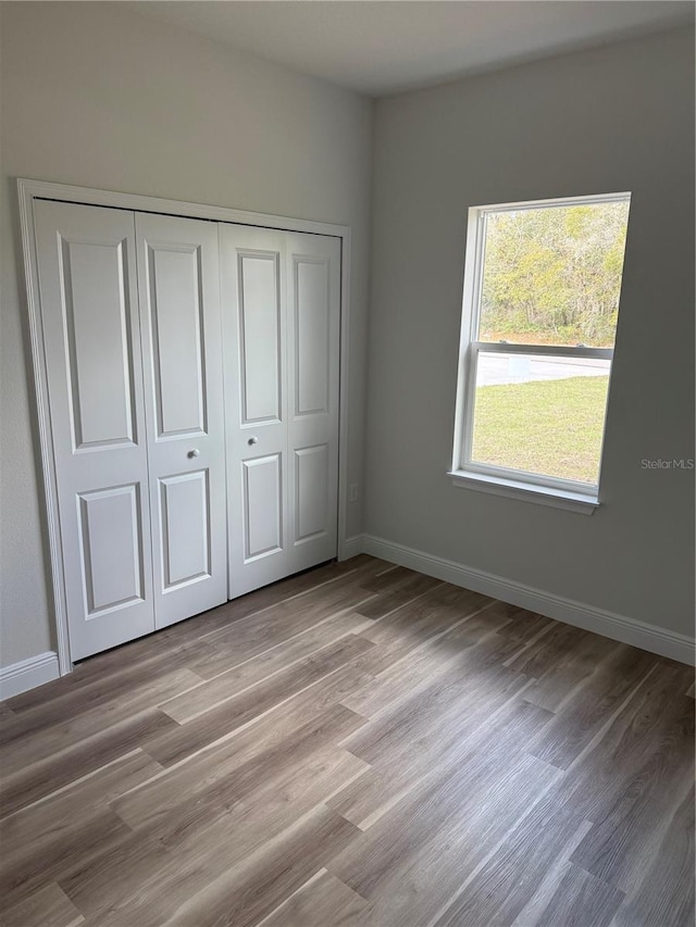 unfurnished bedroom featuring light wood-style flooring, baseboards, and a closet