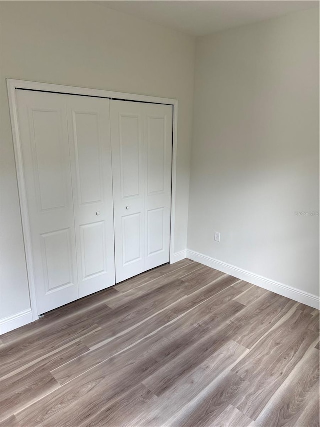 unfurnished bedroom with light wood-style flooring, baseboards, and a closet