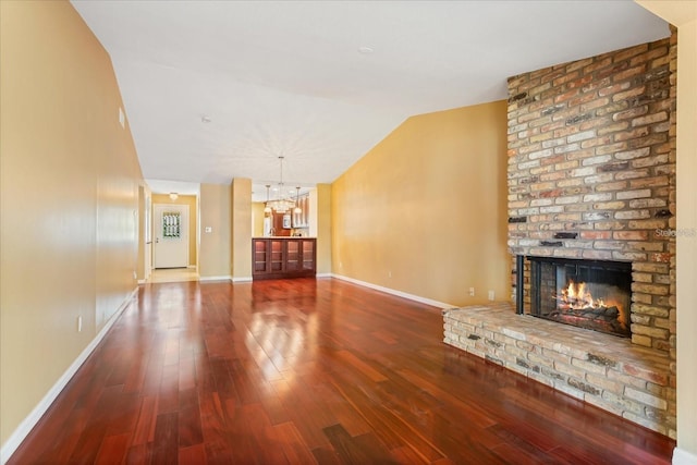 unfurnished living room with lofted ceiling, a brick fireplace, wood finished floors, a chandelier, and baseboards