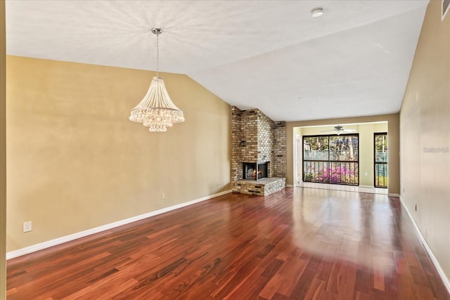 unfurnished living room featuring lofted ceiling, a brick fireplace, wood finished floors, baseboards, and ceiling fan with notable chandelier