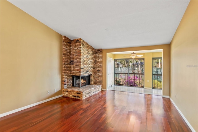 unfurnished living room featuring a brick fireplace, wood finished floors, a ceiling fan, and baseboards