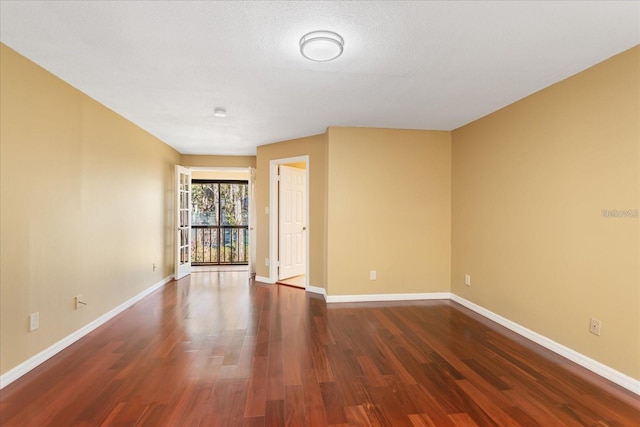 empty room with a textured ceiling, baseboards, and dark wood-style flooring