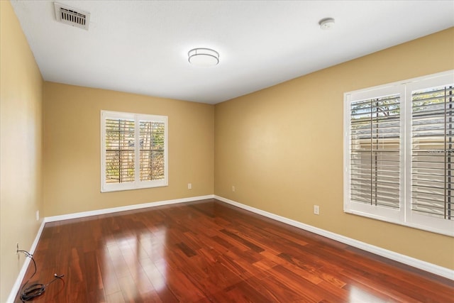 spare room with baseboards, visible vents, and dark wood finished floors