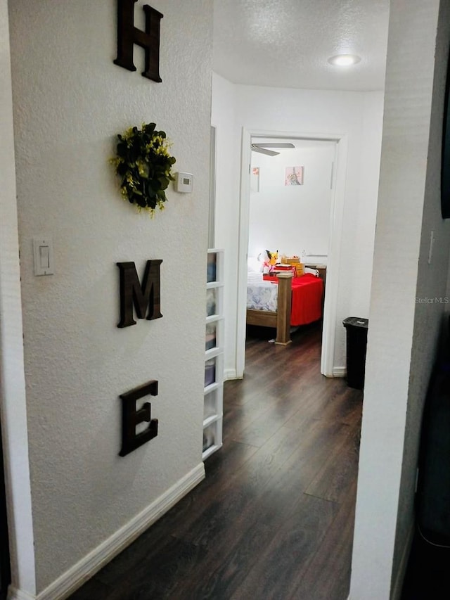 hallway with baseboards, dark wood finished floors, a textured ceiling, and a textured wall