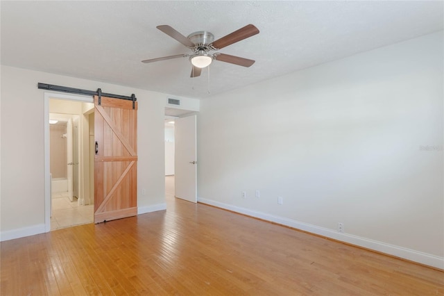 unfurnished room with a barn door, baseboards, a ceiling fan, a textured ceiling, and light wood-style floors