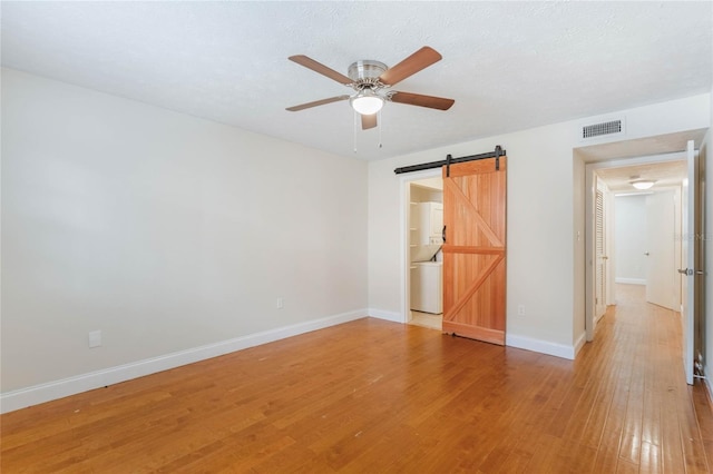 unfurnished room featuring visible vents, light wood-style flooring, a barn door, ceiling fan, and baseboards
