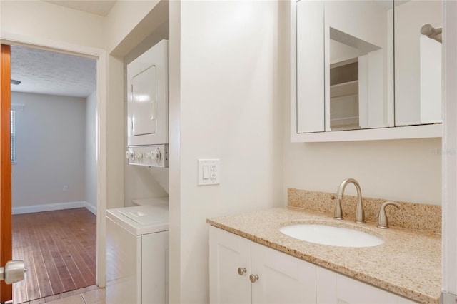 bathroom featuring baseboards, vanity, stacked washing maching and dryer, and a textured ceiling