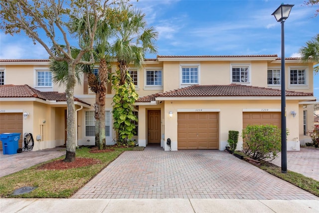 view of property with decorative driveway, an attached garage, a tile roof, and stucco siding