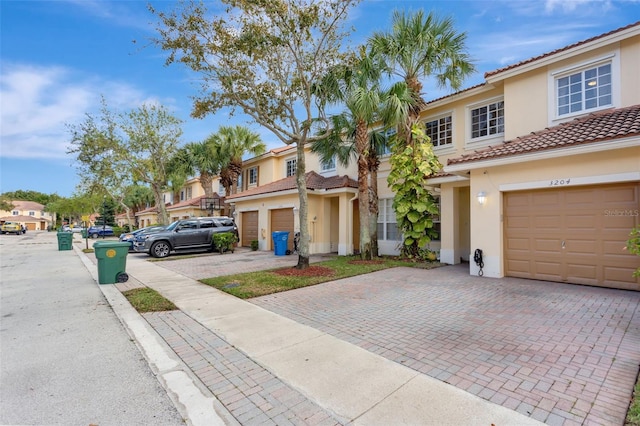 townhome / multi-family property with a garage, driveway, a tile roof, a residential view, and stucco siding