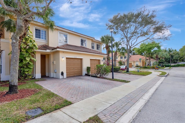 townhome / multi-family property featuring decorative driveway, a tile roof, stucco siding, an attached garage, and a residential view