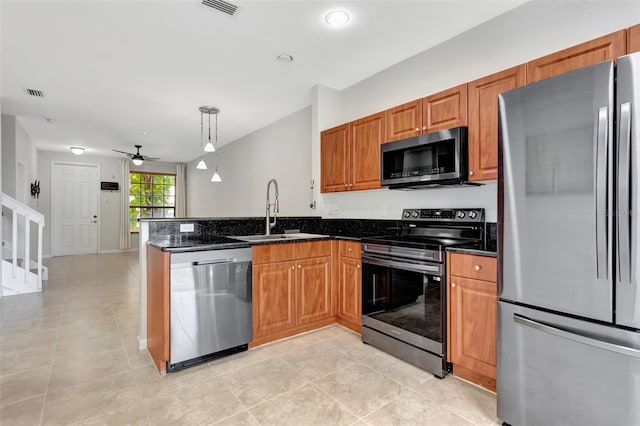 kitchen with brown cabinetry, dark stone counters, decorative light fixtures, stainless steel appliances, and a sink