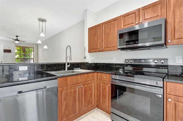 kitchen featuring brown cabinets, hanging light fixtures, appliances with stainless steel finishes, a sink, and dark stone counters