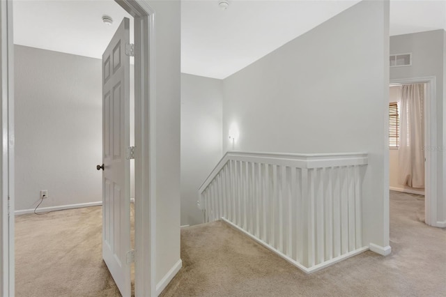 hall with light carpet, baseboards, and visible vents