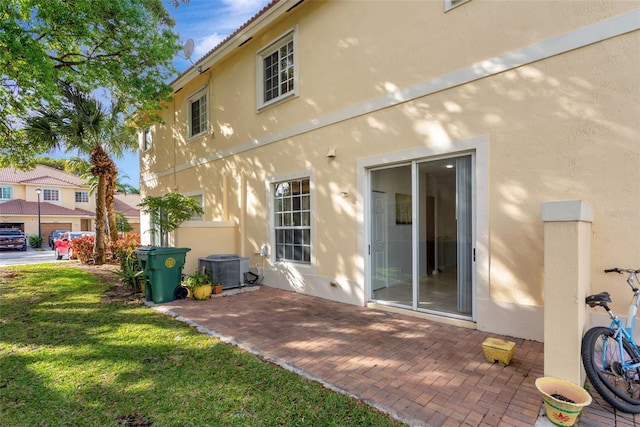 rear view of house featuring central air condition unit, a patio area, a lawn, and stucco siding