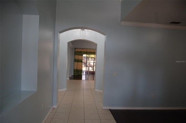 hallway with arched walkways, light tile patterned floors, ornamental molding, and baseboards