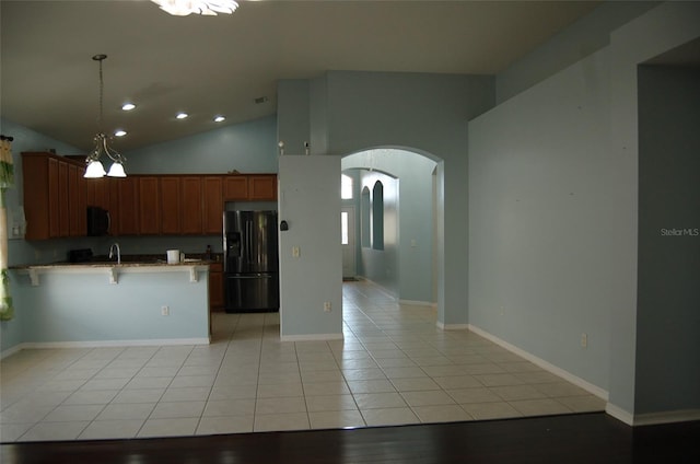 kitchen featuring arched walkways, a breakfast bar, a peninsula, black fridge, and light tile patterned flooring