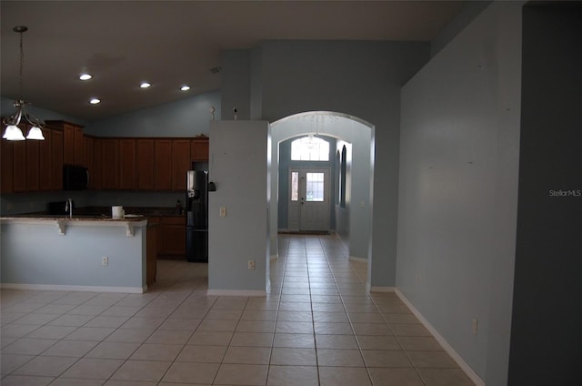 kitchen featuring arched walkways, light tile patterned floors, a sink, black appliances, and a kitchen breakfast bar