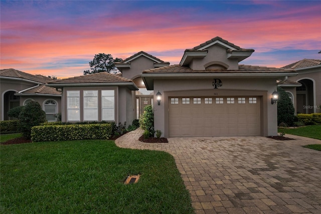 mediterranean / spanish house with a garage, stucco siding, decorative driveway, and a yard