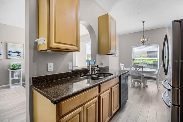 kitchen featuring dark stone counters, dishwashing machine, light wood-style flooring, freestanding refrigerator, and a sink