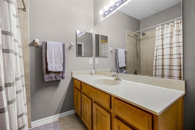 bathroom with tile patterned flooring, tiled shower, vanity, and baseboards