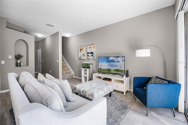 living area with wood finished floors, visible vents, baseboards, and stairs