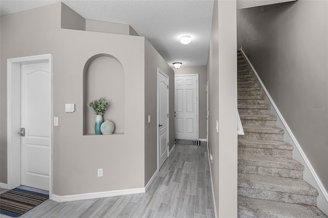 staircase featuring a textured ceiling, baseboards, and wood finished floors