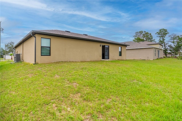 rear view of property with cooling unit, a lawn, and stucco siding