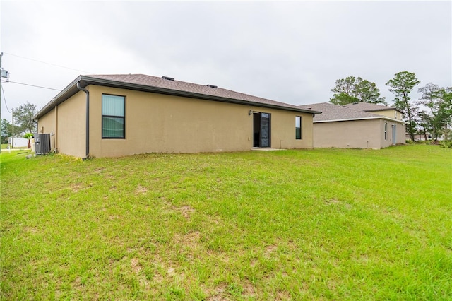 rear view of property with central air condition unit, stucco siding, and a yard