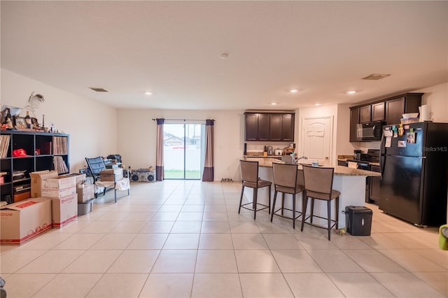 kitchen featuring a breakfast bar area, visible vents, open floor plan, light tile patterned flooring, and black appliances