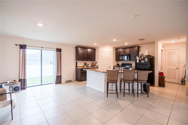 kitchen with dark brown cabinetry, recessed lighting, a breakfast bar, black appliances, and an island with sink