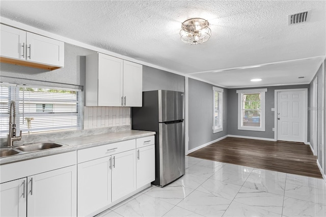 kitchen featuring marble finish floor, white cabinets, a sink, and freestanding refrigerator