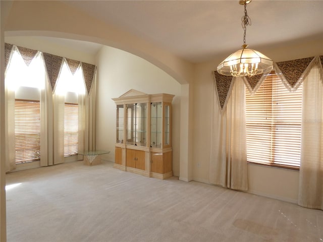 spare room featuring carpet floors, arched walkways, and a chandelier