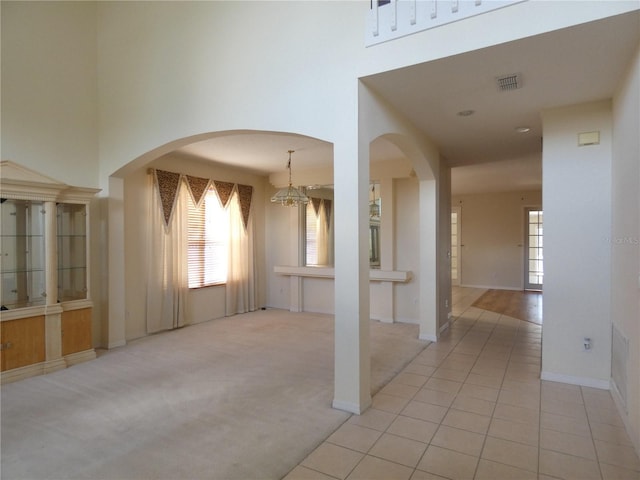 unfurnished room with a towering ceiling, light tile patterned flooring, visible vents, and light colored carpet