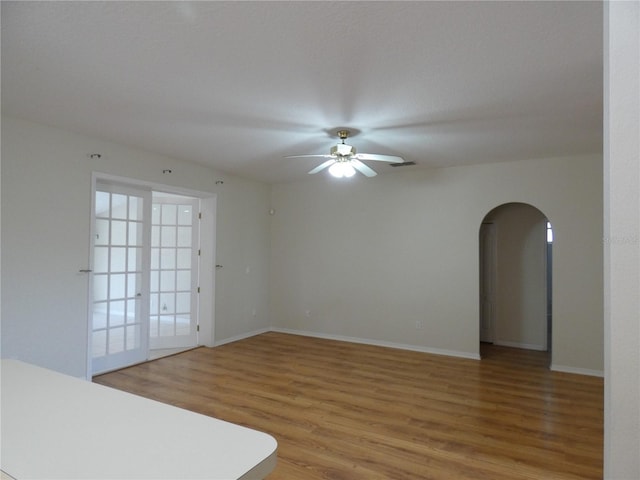 unfurnished room with light wood-style floors, arched walkways, ceiling fan, and baseboards