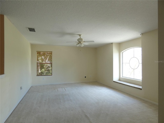 spare room with ceiling fan, visible vents, a textured ceiling, and light colored carpet