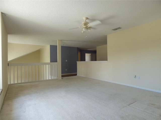 empty room with a textured ceiling, ceiling fan, light colored carpet, visible vents, and baseboards