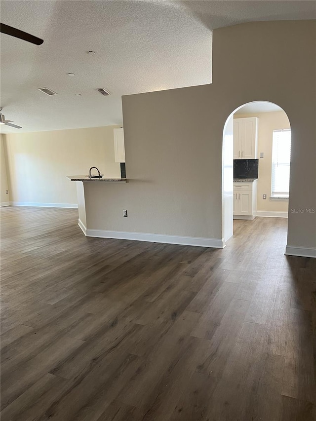 unfurnished room with arched walkways, visible vents, dark wood finished floors, and ceiling fan