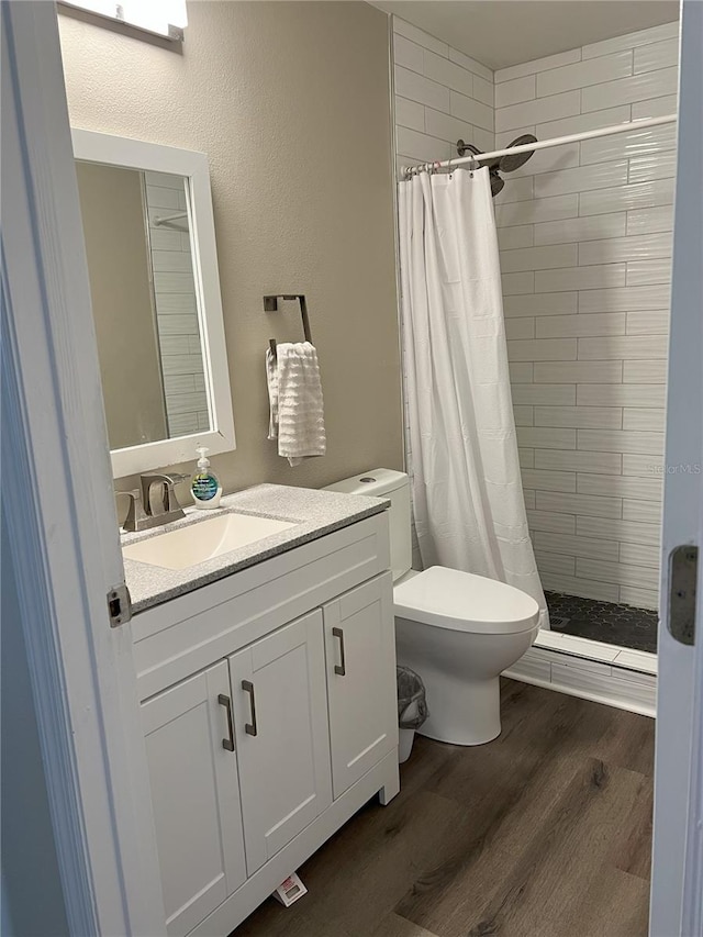 bathroom with a stall shower, toilet, wood finished floors, and vanity