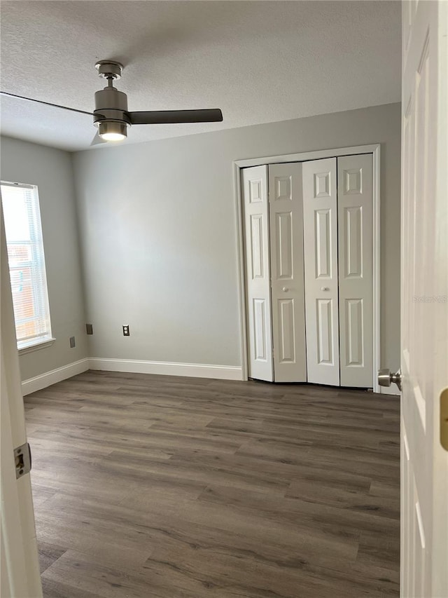 unfurnished bedroom with dark wood finished floors, a closet, a textured ceiling, and baseboards