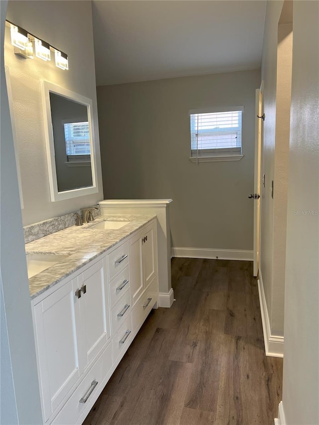 full bathroom featuring double vanity, wood finished floors, baseboards, and a sink