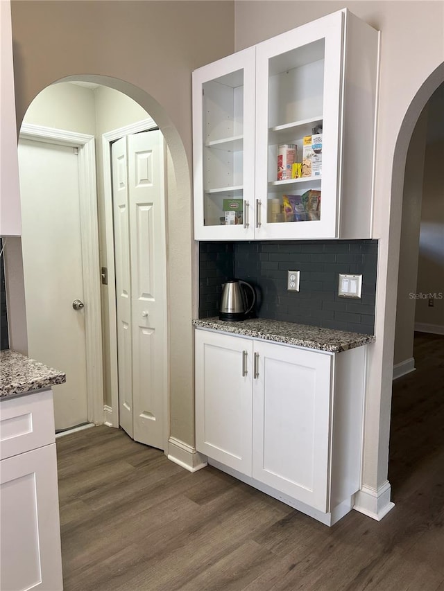 bar featuring baseboards, arched walkways, backsplash, and dark wood-style flooring